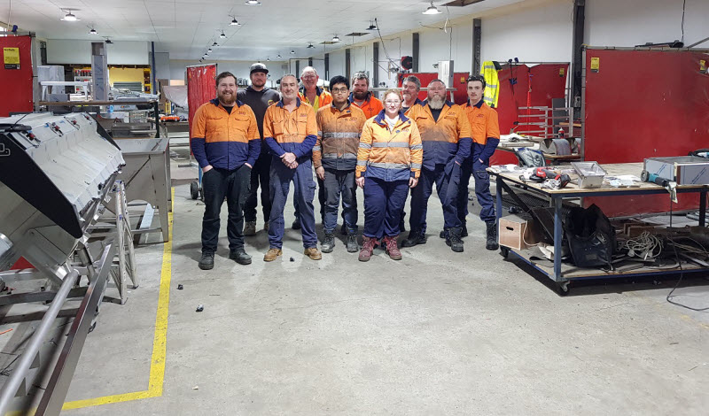 Team of workers wearing orange uniform smiling at the camera while working in the warehouse